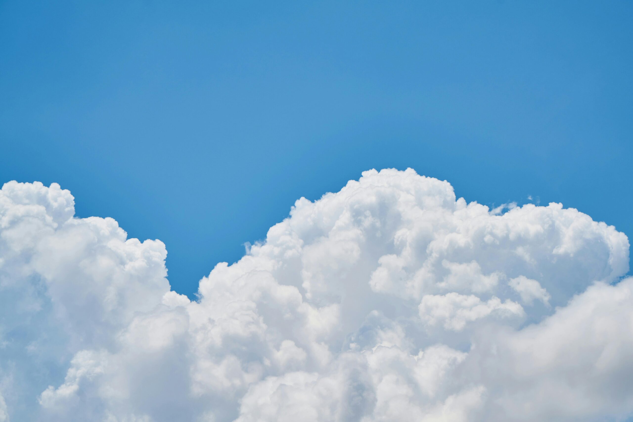 Bright blue sky with large, fluffy white clouds rising high into the atmosphere, creating a vibrant and serene scene.